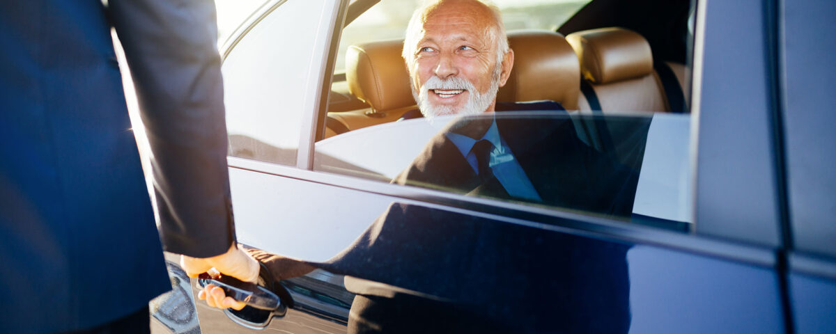 Business traveler exiting a luxury vehicle with chauffeur assistance for corporate car service to the airport.