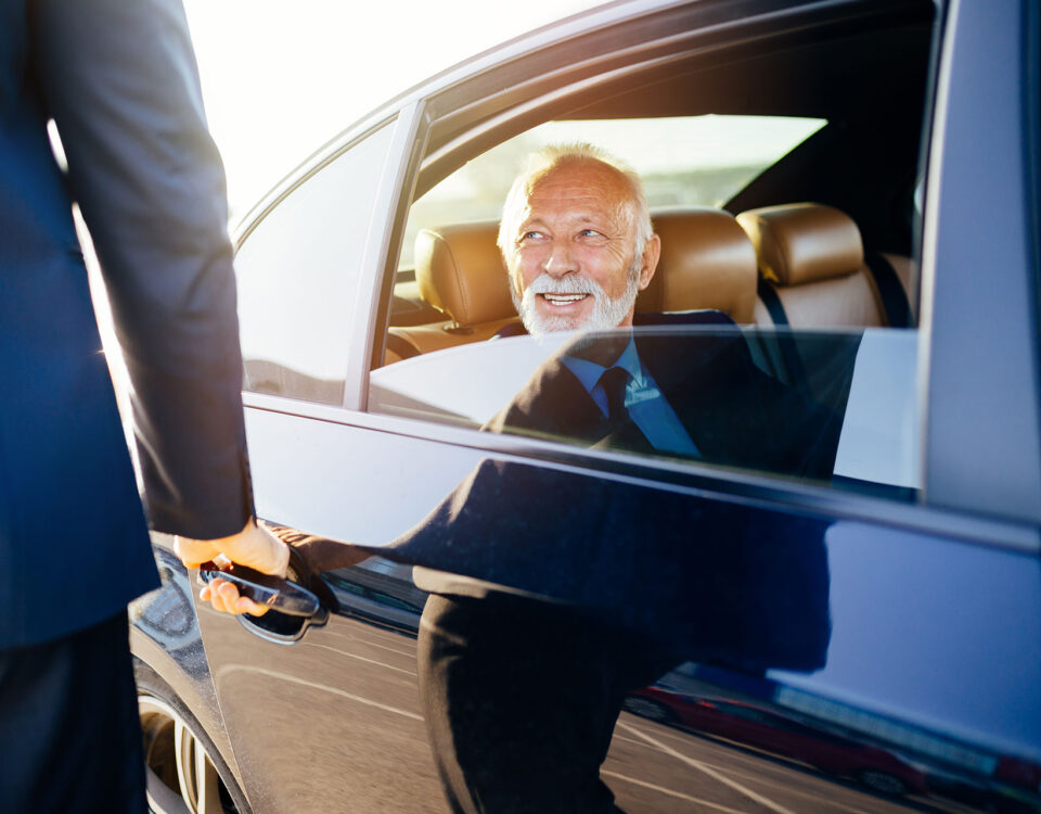 Business traveler exiting a luxury vehicle with chauffeur assistance for corporate car service to the airport.